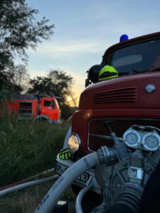 Feuerwehrauto mit Schläuchen bei Sonnenuntergang.