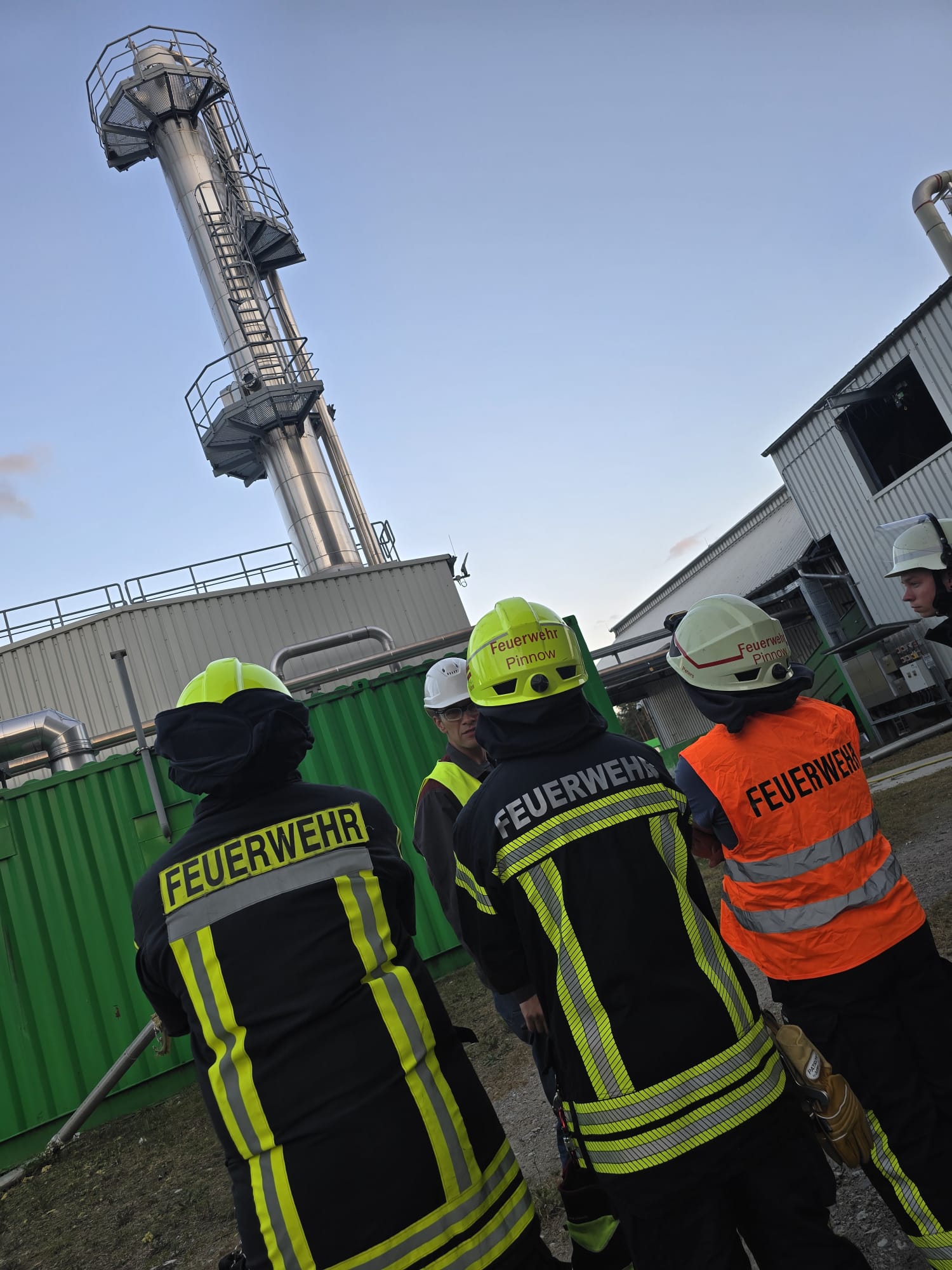 Feuerwehrleute vor einer Industrieanlage bei klarem Himmel