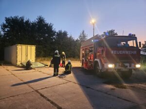 Feuerwehrübungs: Container und Löschfahrzeug bei Dämmerung