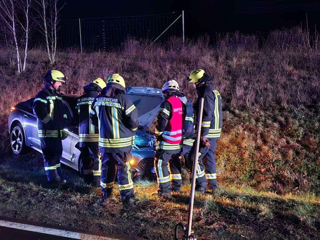 Feuerwehrleute untersuchen Auto im Graben nachts.