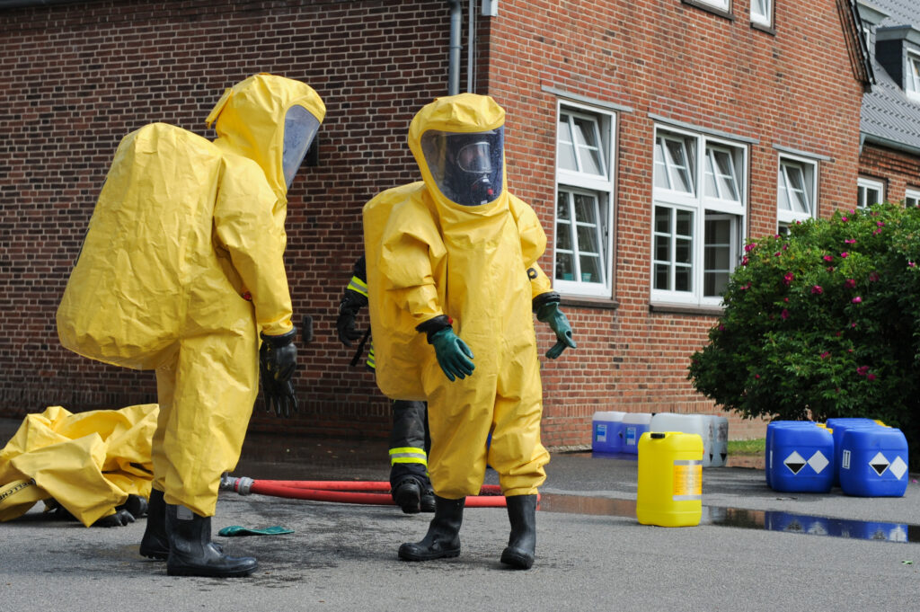 Personen in gelben Schutzanzügen vor Ziegelgebäude